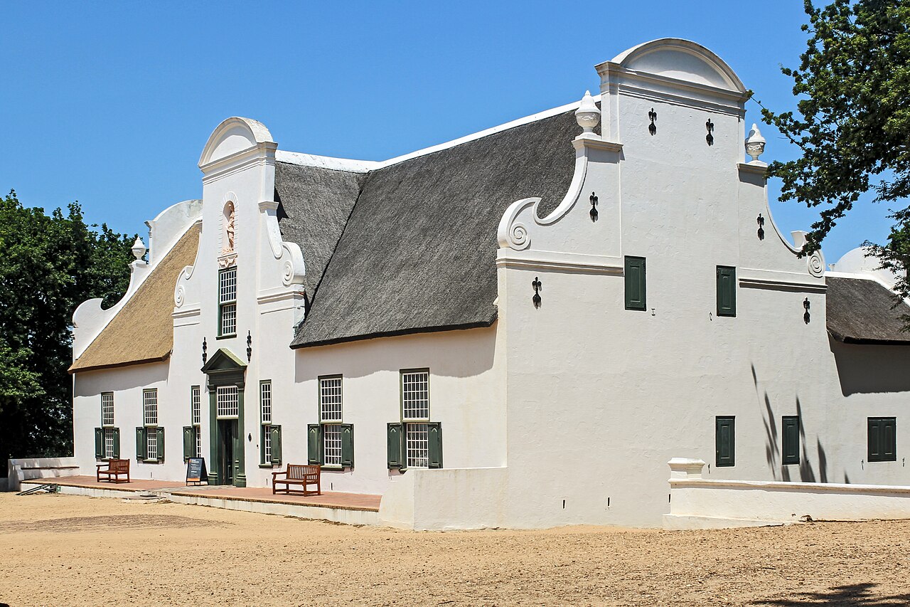 Historic whitewashed Cape Dutch homestead with thatched roof and curved ornate gables